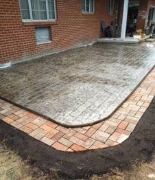 Concrete patio with surrounding brick border next to a brick house.
