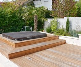 Holzterrasse mit Whirlpool und Garten, umgeben von Pflanzen und einer Mauer im modernen Design.