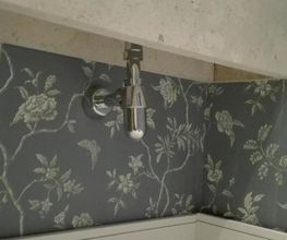 Baño con papel tapiz floral gris y grifo metálico en pared decorada.