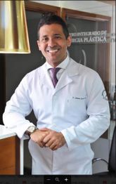 Não sei quem é na imagem. Médico sorrindo, vestindo jaleco branco, em consultório moderno.