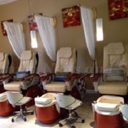 Four empty pedicure chairs with foot spas in a well-lit salon.