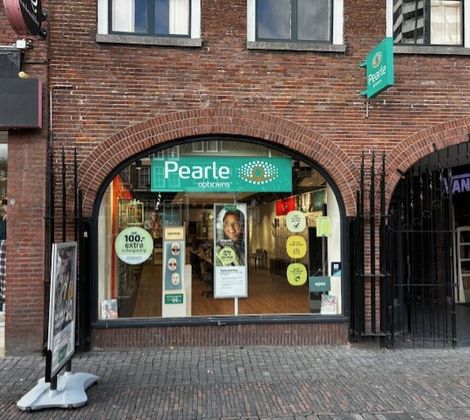 Gevel van een Pearle opticienwinkel in een bakstenen gebouw, met diverse posters en logo's.