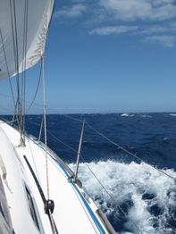 Segelboot auf stürmischer See unter blauem Himmel und Wolken.
