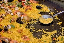 Paella mit Meeresfrüchten in einer großen Pfanne und einem Servierlöffel aus Metall.
