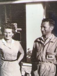 Una donna e un uomo sorridenti in abiti vintage, all'aperto davanti a un edificio.