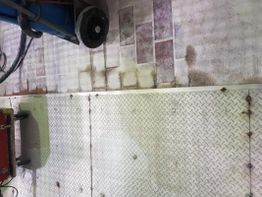 Metallboden mit Schmutz- und Reifenabdrücken, daneben ein Reinigungsgerät und Schläuche.