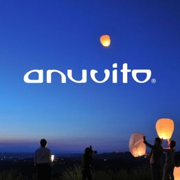 Menschen lassen bei Sonnenuntergang Himmelslaternen steigen; Schriftzug "anuvito" darüber.