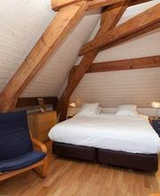 Dachgeschoss-Schlafzimmer mit Holzbalken, Doppelbett und Sessel auf Holzboden.