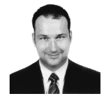 Schwarz-weiß-Foto eines lächelnden Mannes im Anzug mit Krawatte, von vorne aufgenommen.