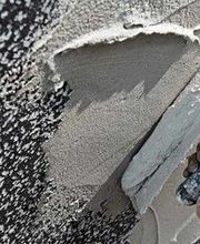 Hand verputzt eine Wand mit grauem Mörtel.