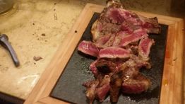 Bistecca alla fiorentina su tagliere di legno, cotta al sangue, su tavolo di marmo.