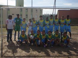 Time juvenil de futebol posando em um campo de terra, com uniformes azuis e amarelos.