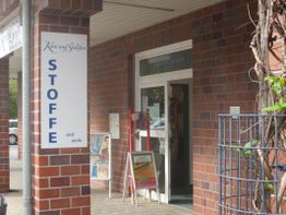 Geschäftseingang mit Schild "Stoffe und mehr" an einer Ziegelfassade.