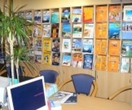 Reisebüro mit Broschürenwand, Computer und Pflanze auf einem Tisch.