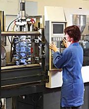 Person bedient Maschine in einer Fabrik. Trägt blauen Kittel und steht an der Steuerkonsole.