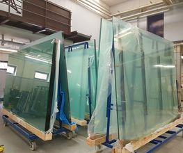 Große Glasplatten auf Rollwagen in einer Lagerhalle, bereit für den Transport.