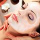 Woman with a facial mask relaxing during a spa treatment, eyes closed, hands gently on her neck.