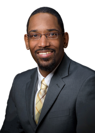 Smiling man in a gray suit and glasses with a patterned tie, posing against a black background.