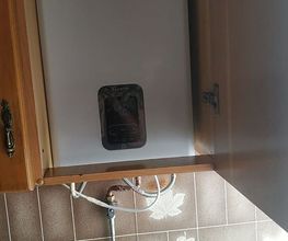 Calentador de agua blanco en un gabinete de cocina con recipiente azul debajo.