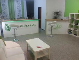 Heller Verkaufsraum mit Tresen, Barhockern und Regalen, grün-weiße Dekoration.