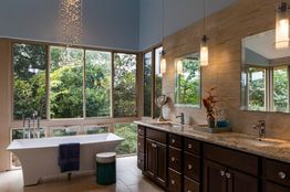 Modern bathroom with a freestanding tub, large windows, and a wooden vanity with pendant lights.