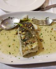 Plato con filete de pescado en salsa verde, acompañado de una cuchara y un tenedor.