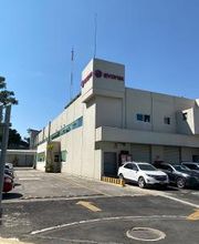 Edificio blanco con cartel en el techo, rodeado de autos estacionados en un día soleado.