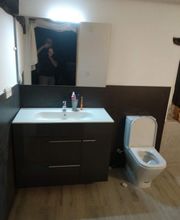 Baño moderno con lavabo, espejo, inodoro y reflejo de persona tomando la foto visible en el espejo.