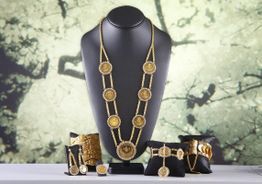 Goldene Schmuckkollektion auf schwarzem Display vor abstraktem Hintergrund.