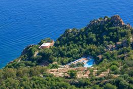 Veduta aerea di una località montuosa con vegetazione lussureggiante e vista sul mare blu.