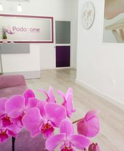 Sala de espera moderna con sofá lila y orquídeas rosas. Cartel: "Podo One".