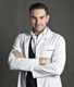 Uomo in camice bianco, con le braccia incrociate, sfondo grigio.