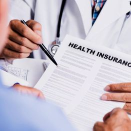 Doctor discusses health insurance form with a patient, pointing with a pen.