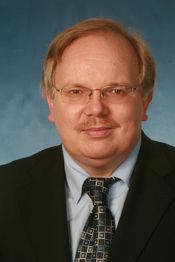 Mann mit Brille und Anzug vor blauem Hintergrund.