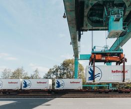 Carga de contenedores en un tren bajo una grúa en estación de transporte intermodal.