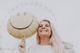 Smiling woman holding a yellow smiley balloon with a ferris wheel in the blurry background.