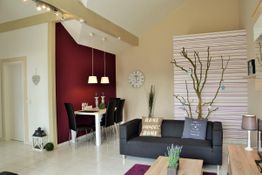 Modernes Wohnzimmer mit schwarzem Sofa, roter Wand, Esstisch und minimalistischer Dekoration.
