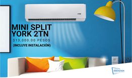 Aire acondicionado Mini Split York 2TN en pared azul, sofá con cojines y lámpara amarilla.