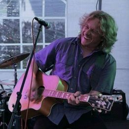 Mann spielt Gitarre und singt leidenschaftlich auf der Bühne.