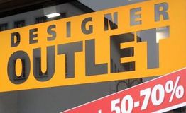 "Schaufenster mit gelbem 'Designer Outlet'-Schild, rotes Schild mit 50-70% Rabatt darunter."