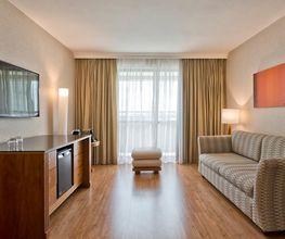 Sala de estar com sofá, TV, cortinas, luminária e piso de madeira. Móveis em tons neutros.