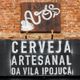 Placa de "Cerveja artesanal da Vila Ipojuca" em parede de tijolos.