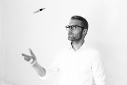 Mann in Hemd und Brille wirft einen Stift in die Luft.