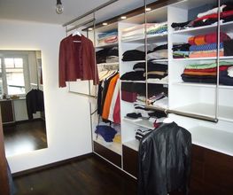 Begehbarer Kleiderschrank mit Kleidung, Spiegel, hängenden Jacken und Regalen voller Kleidung.