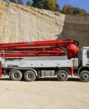 LKW mit rotem Betonpumpenausleger steht im Steinbruch vor einer Felswand.