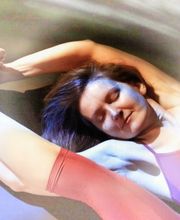 Frau in rosa Outfit macht Yoga-Übung, dehnt sich mit geschlossenen Augen auf bunter Unterlage.