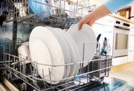 Person loading white plates into a dishwasher rack in a kitchen.