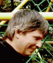 Person lächelt vor einem Klettergerüst mit gelben und grünen Seilen im Hintergrund.