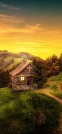 Kleine Holzhütte in hügeliger Landschaft bei Sonnenuntergang, umgeben von Bäumen und Wiesen.