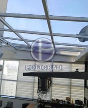 Espaço interno com teto de vidro e móveis, observando prédios ao fundo.